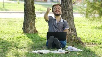 joven Universidad enano estudiante mirando a ordenador portátil al aire libre en parque es exitoso y contento. video