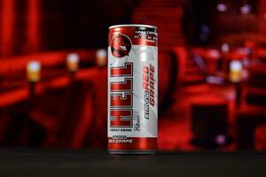 KHARKOV, UKRAINE - FEBRUARY 14, 2021 Hell energy drink can on black wooden table with red interior background photo