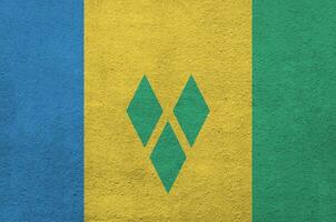 Saint Vincent and the Grenadines flag depicted in bright paint colors on old relief plastering wall. Textured banner on rough background photo