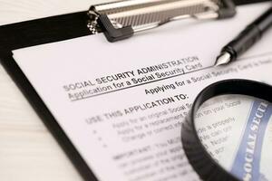 United States social security number cards lies on Application from social security administration on A4 tablet lies on office table with pen and magnifying glass photo