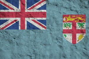 Fiji flag depicted in bright paint colors on old relief plastering wall. Textured banner on rough background photo