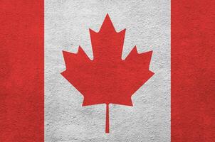 Canada flag depicted in bright paint colors on old relief plastering wall. Textured banner on rough background photo