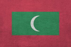 Maldives flag depicted in bright paint colors on old relief plastering wall. Textured banner on rough background photo