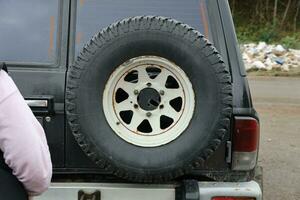 Wheel closeup in a countryside landscape with a mud road. Off-road 4x4 suv automobile with ditry body after drive in muddy road photo