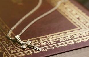 Silver necklace with crucifix cross on christian holy bible book on black wooden table. Asking blessings from God with the power of holiness, which brings luck photo