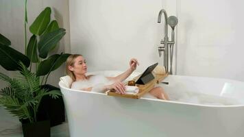 uma mulher relaxa enquanto deitado dentro a banheira e usa uma digital tábua. video