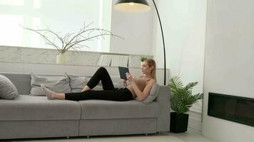 ein Frau Verwendet ein Tablette während Lügen auf das Sofa beim heim. video