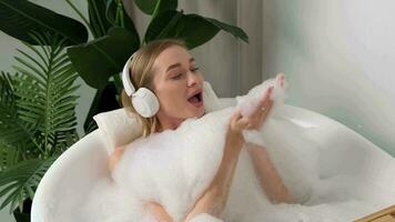 un mujer vistiendo auriculares escucha a música mientras acostado en el bañera durante agua procedimientos. video