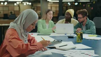 criativo muçulmano o negócio mulher trabalhando em uma projeto dentro a escritório sentado às a mesa Próximo para colegas.diferentes raças, diversas pessoas, criativas equipe, negócios parceiros video