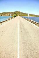 a long empty road with a bridge over the water photo