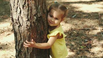 une 2 ans enfant câlins une arbre tronc dans le forêt.terre jour, enregistrer planète, enregistrer le monde, l'amour la nature. video