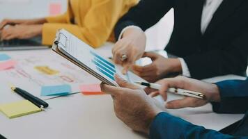 Two creative business people meeting and planning use post it notes sticky note on desk to share idea, Analysis data chart and graph with teamwork strategy brainstorming in office. video