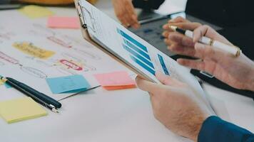 två kreativ företag människor möte och planera använda sig av posta den anteckningar klibbig notera på skrivbord till dela med sig aning, analys data Diagram och Graf med lagarbete strategi brainstorming i kontor. video