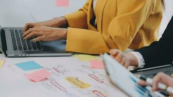 två kreativ företag människor möte och planera använda sig av posta den anteckningar klibbig notera på skrivbord till dela med sig aning, analys data Diagram och Graf med lagarbete strategi brainstorming i kontor. video