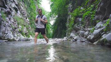 Young adventurous man walking barefoot in rocky creek. video