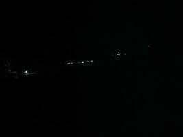 fir trees on meadow between hillsides with conifer forest in fog under the blue sky at night. spooky countryside scenery in full moon light photo