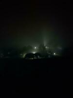 fir trees on meadow between hillsides with conifer forest in fog under the blue sky at night. spooky countryside scenery in full moon light photo