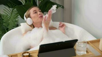 A woman wearing headphones listens to music while lying in the bathtub during water procedures. video