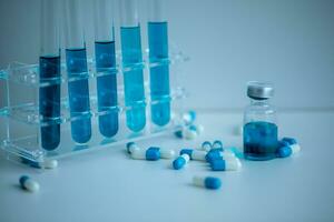 5 blue test tubes placed in the medical tube rack, 1 vaccine vial and several blue-white capsules were scattered around with a white background, Medical concept. photo