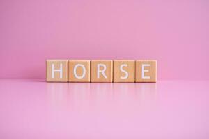 Wooden blocks form the text HORSE against a pink background. photo