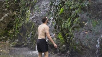 Sporty man stands in front of waterfall. Slow motion. video