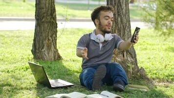 un' maschio Università nano alunno è chat viso tempo con il suo fidanzata nel il parco. video