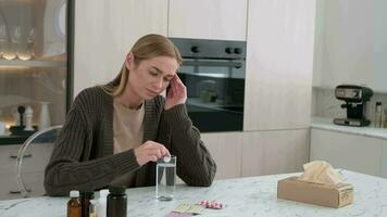 pendant une mal de tête, une femme jette un aspirine tablette dans une verre de l'eau tandis que séance à le table dans le cuisine. video