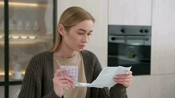 A woman reads the instructions for using pills while sitting at the table at home. video