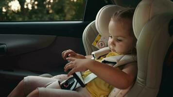 le enfant est assis dans une enfant voiture siège tandis que le voiture est en mouvement et les usages une téléphone intelligent. Voyage concept. video