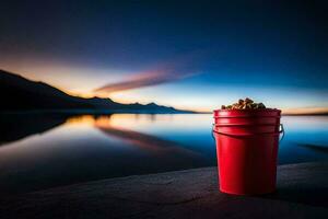 a red bucket sitting on the shore of a lake with a sunset in the background. AI-Generated photo