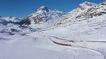 Zug im Schweiz in der Nähe von Bernina bestehen auf sonnig Winter Tag. Bernina Eisenbahn. schweizerisch Alpen. Antenne Sicht. Drohne fliegt rückwärts video