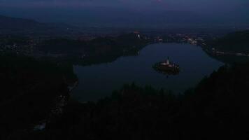 Bled Lake, Illuminated Marijinega Vnebovzetja Church and Blejski Castle at Night. Julian Alps. Slovenia, Europe. Aerial View. Drone Flies Forward, Tilt Up. Reveal Shot video