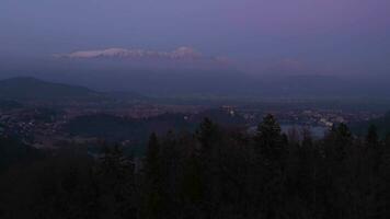 Bled Lake, Illuminated Marijinega Vnebovzetja Church and Blejski Castle at Blue Hour. Julian Alps. Slovenia, Europe. Aerial View. Drone Flies Forward over Trees at Low Level. Reveal Shot video