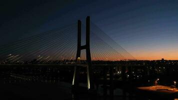 illuminato vasco da gama strallato ponte e Lisbona paesaggio urbano a sera crepuscolo. Lisbona, Portogallo. blu ora. aereo Visualizza. orbitante. largo tiro video