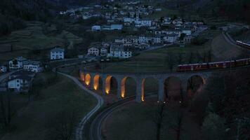 Zug auf beleuchtet brusio Spiral- Viadukt im Schweiz im das Abend. Bernina Eisenbahn. schweizerisch Alpen. Antenne Sicht. umkreisen video