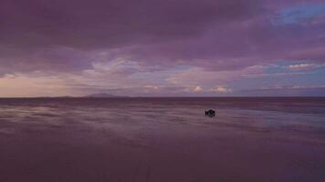 uyuni zout flats en suv auto Bij zonsondergang. antenne visie. hoogvlakte, Bolivia. regenachtig seizoen. tunupa vulkaan. reflectie Aan water in meer oppervlak. dar vliegt vooruit video