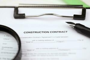 Construction contract form on A4 tablet lies on office table with pen and magnifying glass photo