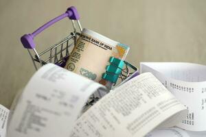 Indian rupees money bills bunch in shopping trolley surrounded by many paper receipts photo