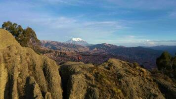 viajante caminhante homem em Colina olhando às la paz paisagem urbana e Illimani montanha. bege Rocha formações. aéreo visualizar. Bolívia. dourado hora. zangão moscas avançar. Largo tomada. estabelecendo tiro video