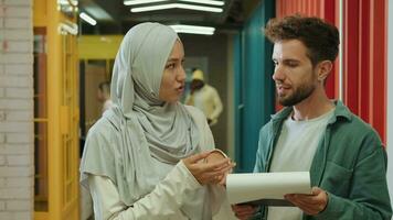 A Muslim business woman and a European businessman are discussing a project while standing in the corridor.Different Races,Diverse People,Creative Team,Business Partners video