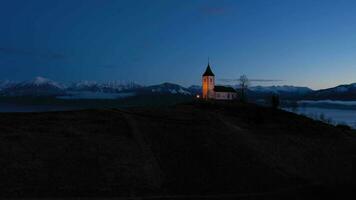 verlichte kerk van st. primo en felicijan in de ochtend- schemering bovenstaand de wolken. julian Alpen. Jamnik, Slovenië, Europa. antenne visie. dar vliegt vooruit en omhoog Bij laag niveau video