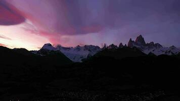 montar Fitz roy, cerro torre y iluminado el castigar pueblo a noche. vistoso nubes colinas y nevadas montañas. Andes, Patagonia, argentina. azul hora. aéreo vista. zumbido moscas hacia atrás video