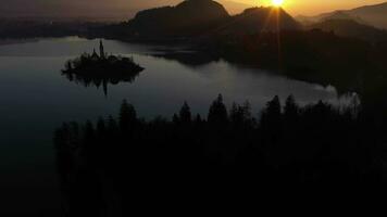 sangrar lago e maconha vnebovzetja Igreja às nascer do sol. dourado hora. colinas e floresta. juliano Alpes. Eslovénia, Europa. reflexão dentro lago. aéreo visualizar. zangão moscas avançar, inclinar acima. revelar tiro video