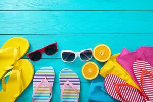 Summer accessories. Flip flops, sunglasses, towels and oranges on blue wooden background. Top view and copy space. photo