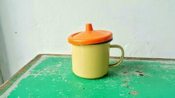 A yellow tin cup with orange lid on the green wooden table photo