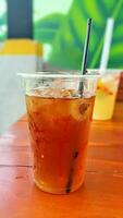 Close up view of a plastic cup of ice tea with straw on the cafe table. Blur background. photo