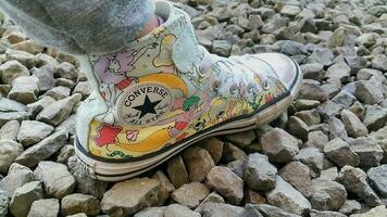 Children's feet wearing sneakers shoes on the pebbles. Colorful pair of Converse shoes on the pebbles. photo