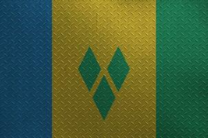Saint Vincent and the Grenadines flag depicted in paint colors on old brushed metal plate or wall closeup. Textured banner on rough background photo