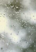 A photo of rain drops on the window glass with a blurred view of the blossoming green trees. Abstract image showing cloudy and rainy weather conditions