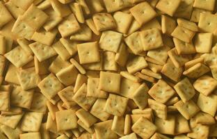 A lot of small cookies are square shaped. A pattern of a yellow salt cracker. Background image with salted pastry photo